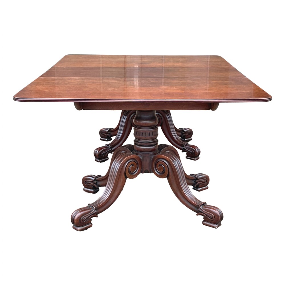 A Regency mahogany twin pillar dining table with an extending centre leaf and carved pedestal supports on brass castors. View V