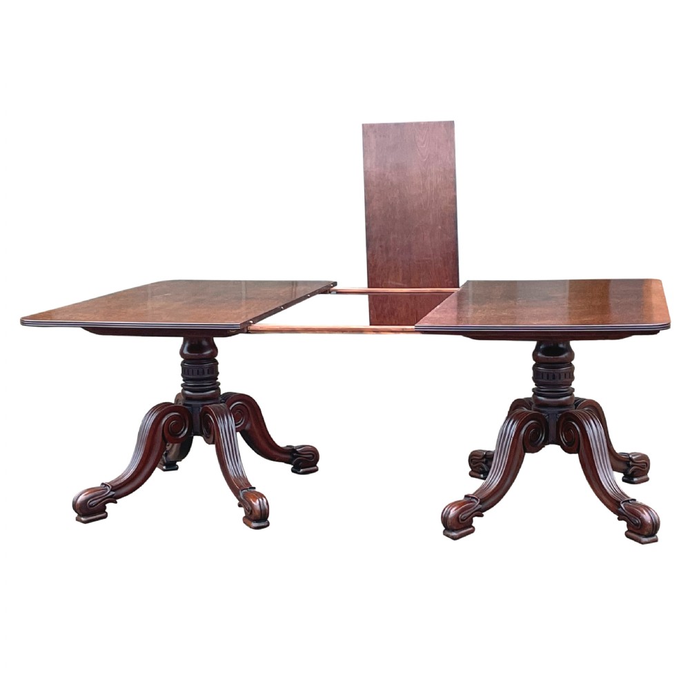 A Regency mahogany twin pillar dining table with an extending centre leaf and carved pedestal supports on brass castors. View VI