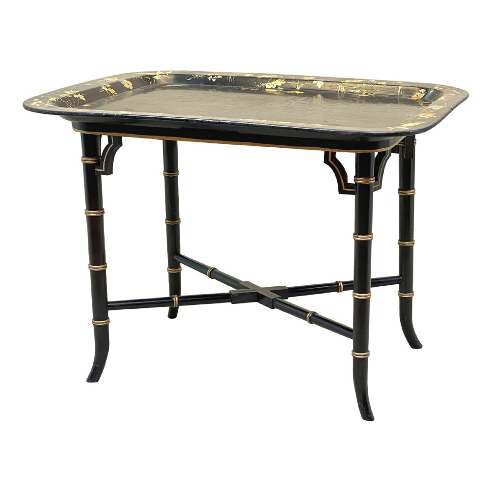 A black lacquered rectangular papier-mache tray table with gilded floral decorations set on ebonised faux bamboo legs.