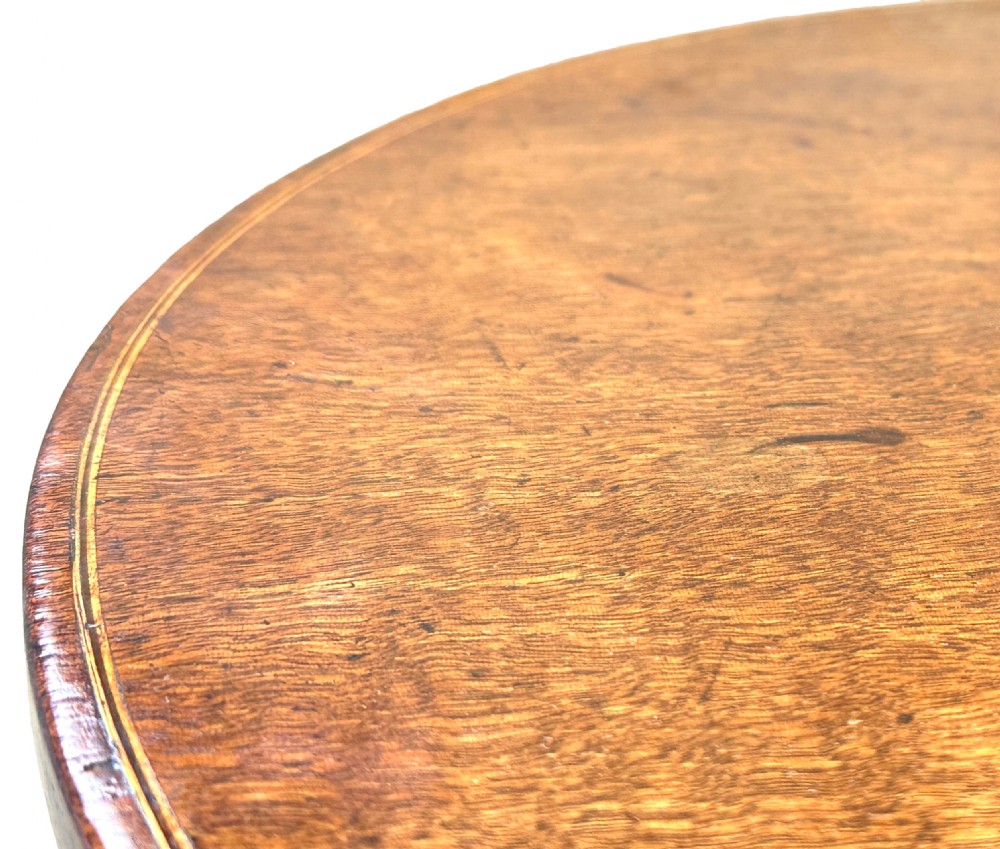 An antique Georgian circular mahogany wine table displayed with its top tilted upwards, supported by a turned pedestal column and a tripod base with three curved legs. View VII