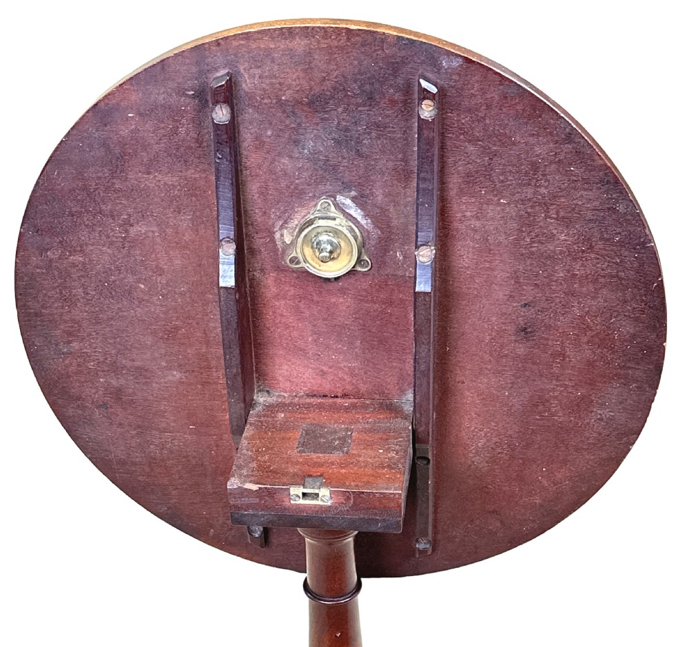 An antique Georgian circular mahogany wine table displayed with its top tilted upwards, supported by a turned pedestal column and a tripod base with three curved legs. View X