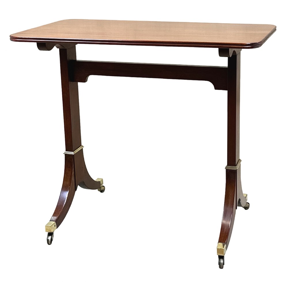 A small Georgian dark mahogany library table featuring a rectangular top, a stretchered trestle base, down-swept sabre legs, and brass castors.