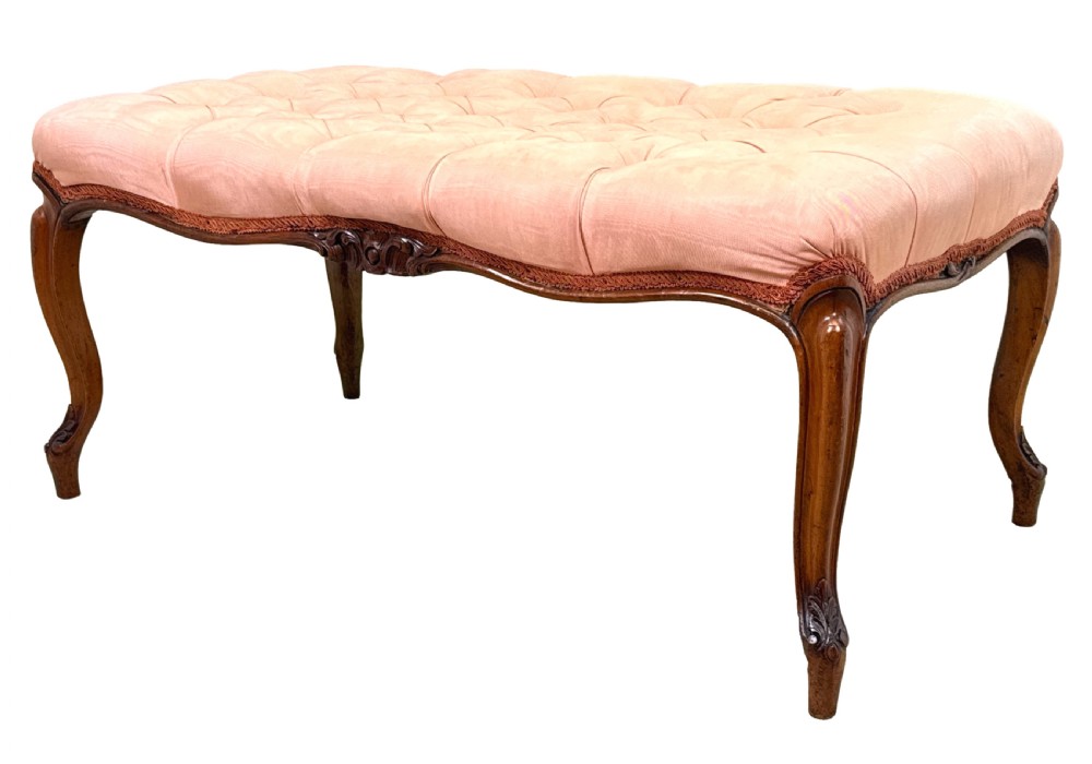 A rectangular Victorian walnut salon stool featuring a button-tufted pink fabric top, carved serpentine apron, and four cabriole legs.