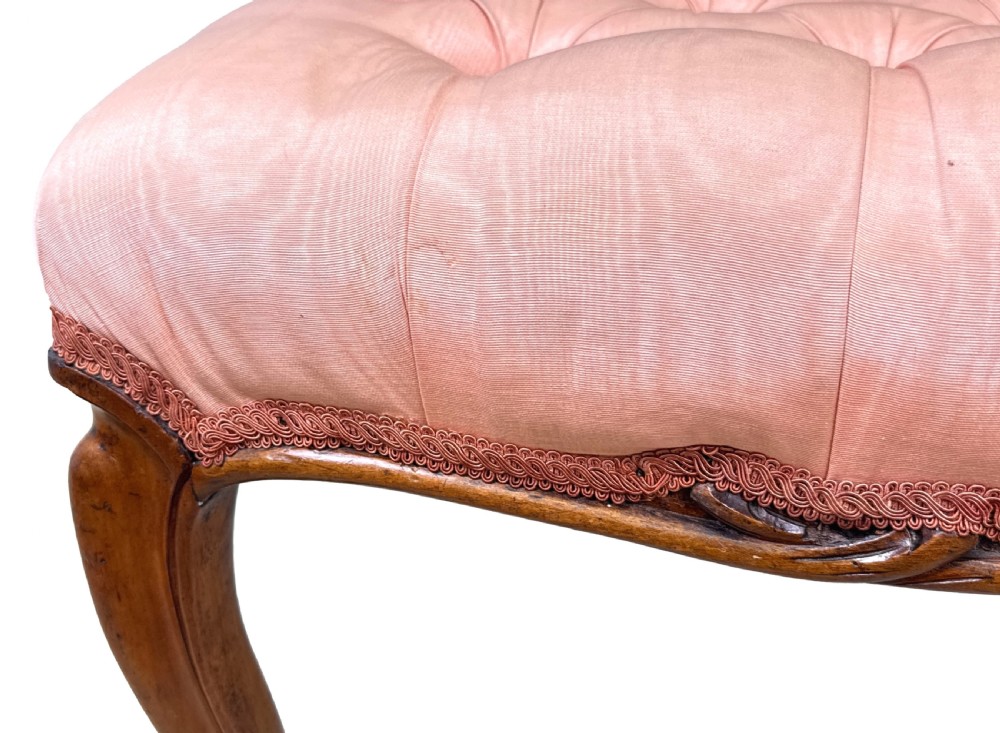 A rectangular Victorian walnut salon stool featuring a button-tufted pink fabric top, carved serpentine apron, and four cabriole legs. View V