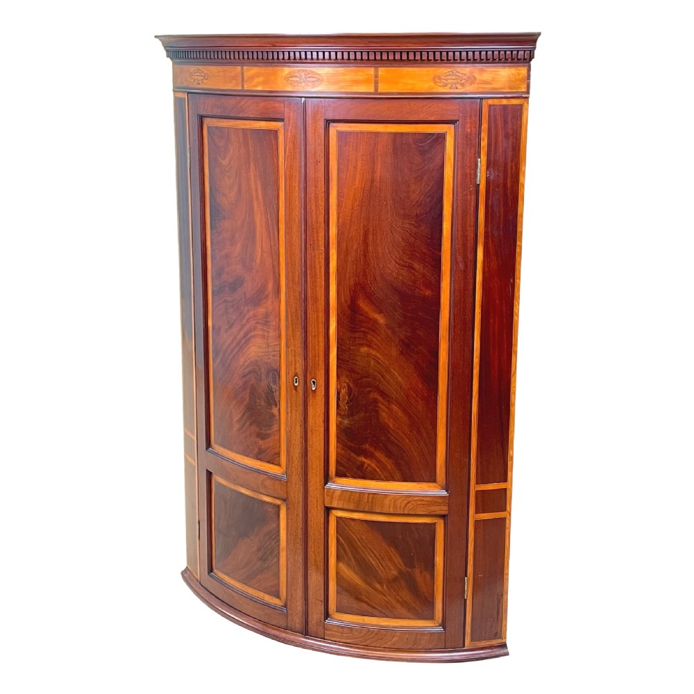 A Georgian bowfront mahogany corner cupboard featuring flame mahogany door panels, classical marquetry inlay, and double doors.