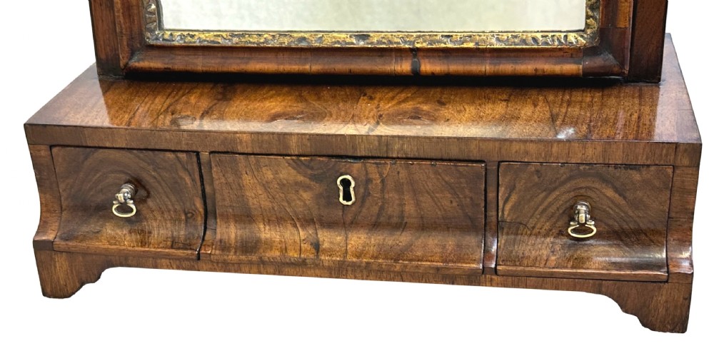 A Georgian walnut dressing table mirror with an adjustable rectangular glass, gilded inner border, and a base containing three concave drawers with brass handles. View VIII