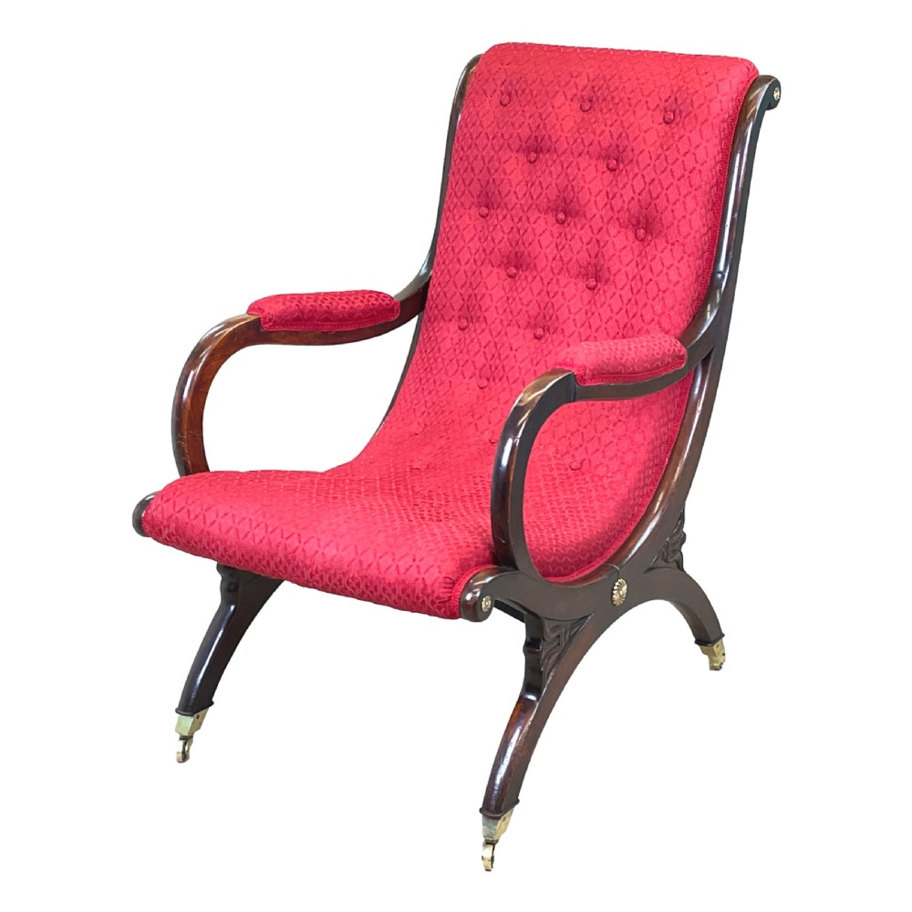 A Regency mahogany library armchair featuring button-backed red upholstery, curved scroll arms, and brass castors.
