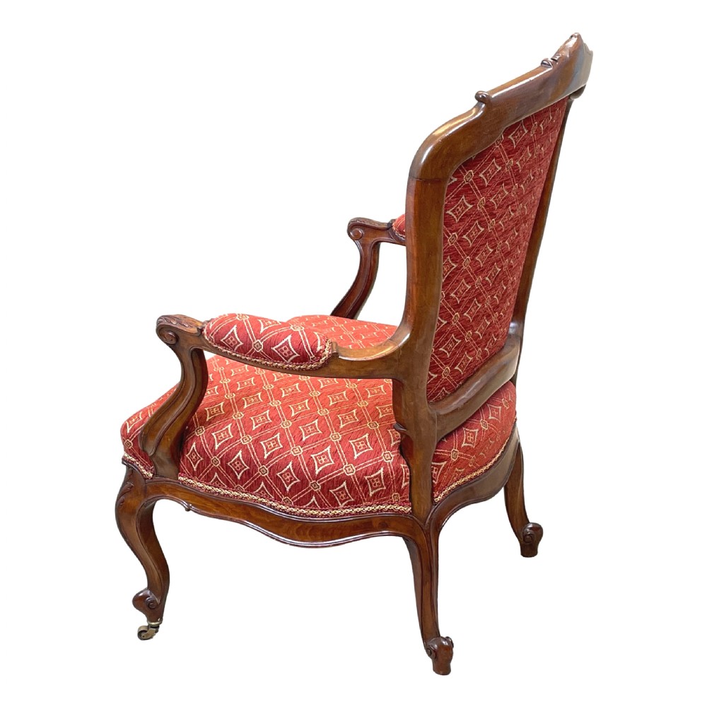 An English 19th-century carved mahogany armchair with red geometric patterned fabric upholstery, padded armrests, cabriole legs, and brass casters. View V
