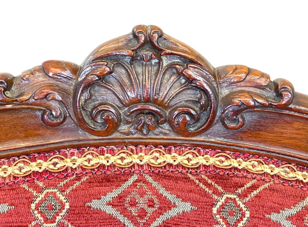 An English 19th-century carved mahogany armchair with red geometric patterned fabric upholstery, padded armrests, cabriole legs, and brass casters. View VII