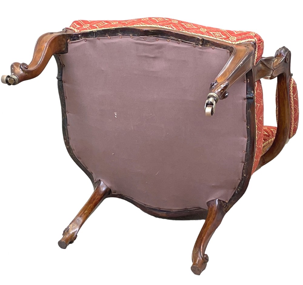 An English 19th-century carved mahogany armchair with red geometric patterned fabric upholstery, padded armrests, cabriole legs, and brass casters. View IX