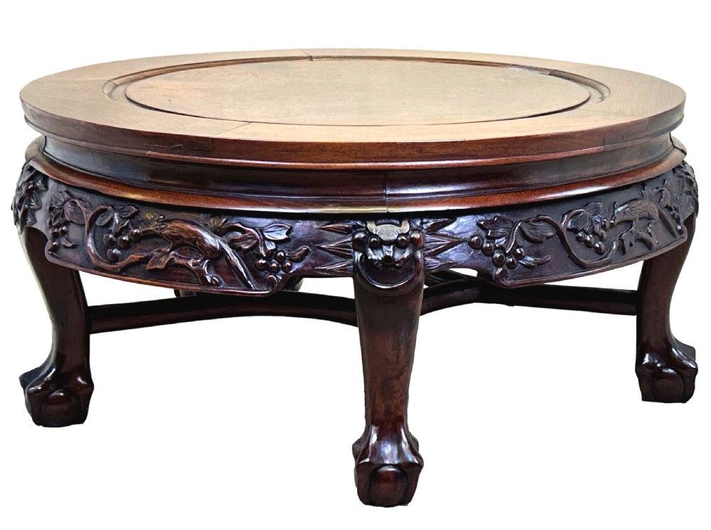 A low circular dark hardwood coffee table featuring hand-carved foliage and animal relief designs along the apron and supported by cabriole legs.