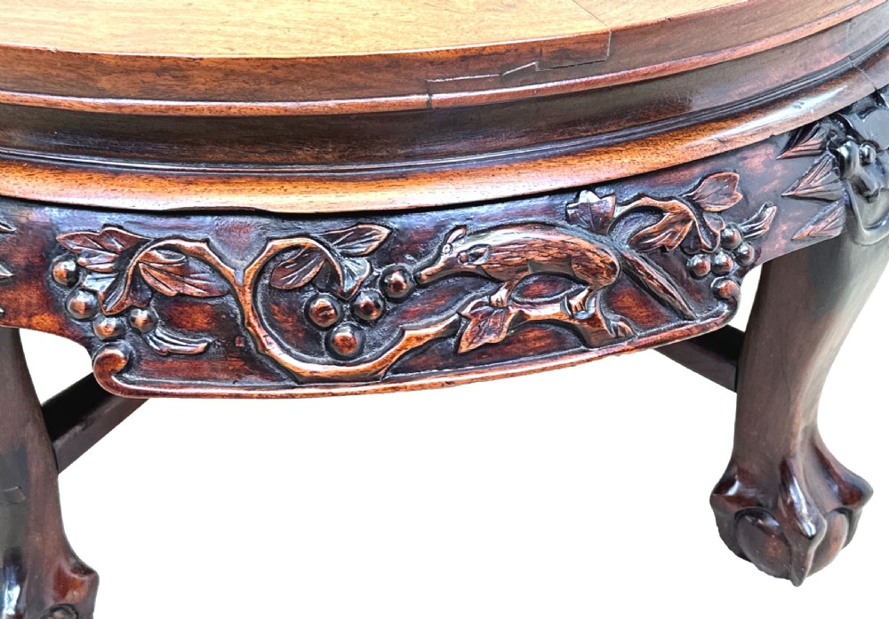 A low circular dark hardwood coffee table featuring hand-carved foliage and animal relief designs along the apron and supported by cabriole legs. View VII
