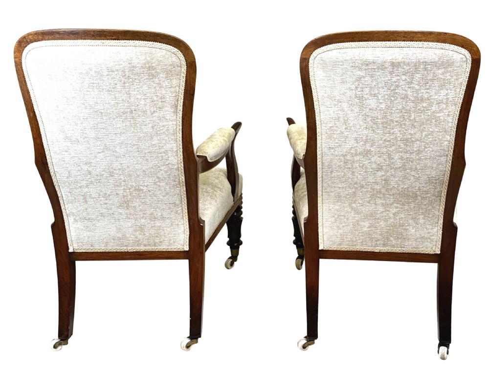 A pair of 19th-century rosewood library armchairs featuring textured beige button-backed upholstery, padded armrests, curved timber supports, turned front legs, and brass castors. View VII