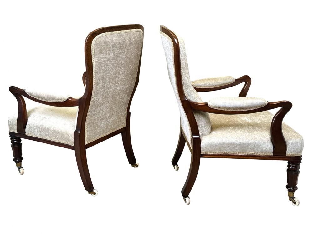 A pair of 19th-century rosewood library armchairs featuring textured beige button-backed upholstery, padded armrests, curved timber supports, turned front legs, and brass castors. View VIII