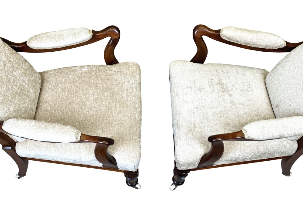 A pair of 19th-century rosewood library armchairs featuring textured beige button-backed upholstery, padded armrests, curved timber supports, turned front legs, and brass castors. View X