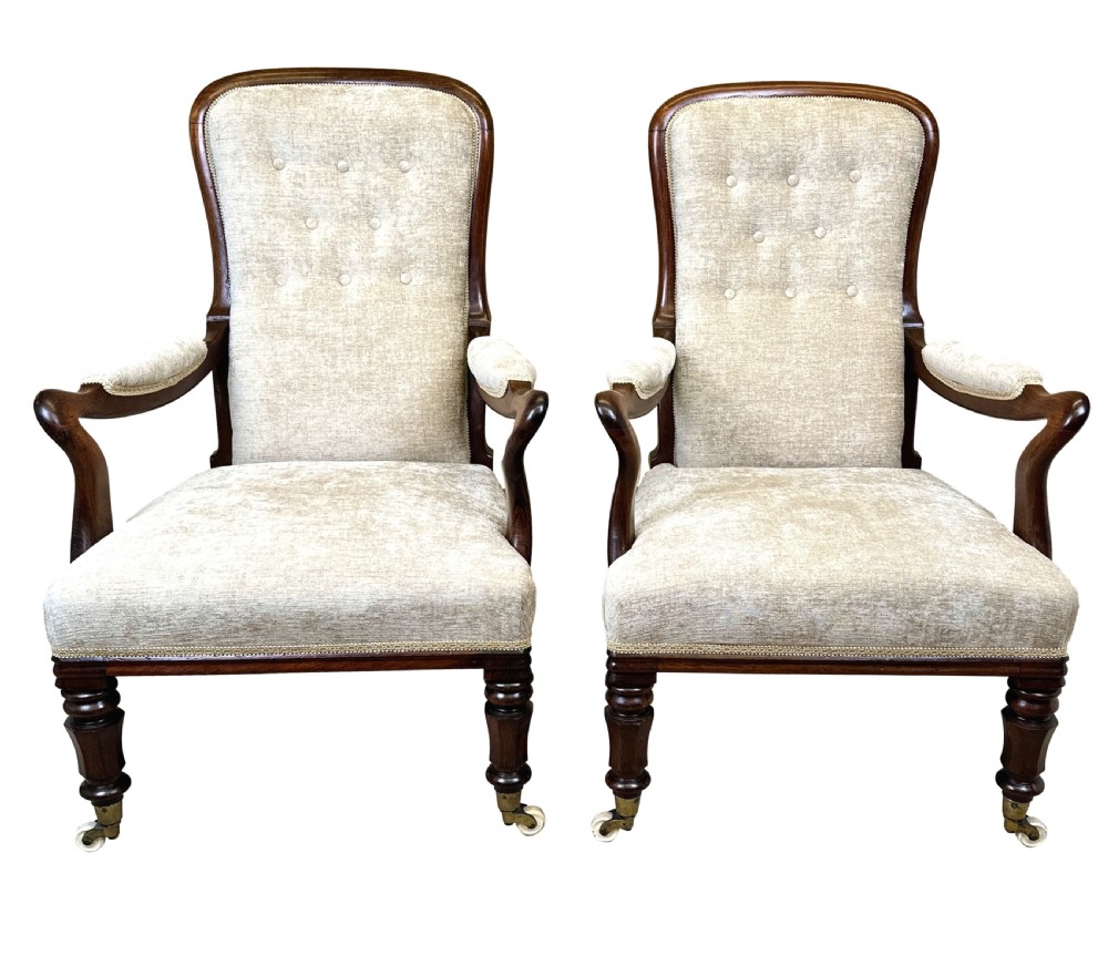 A pair of 19th-century rosewood library armchairs featuring textured beige button-backed upholstery, padded armrests, curved timber supports, turned front legs, and brass castors. View XI