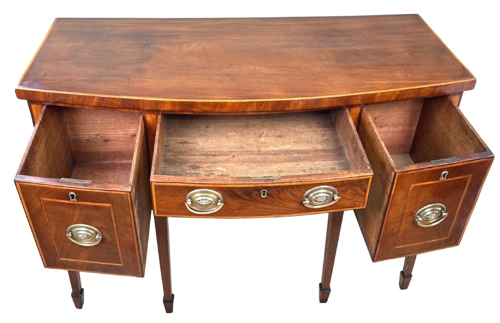 An 18th-century Georgian mahogany bowfront sideboard featuring a gently curved front, satinwood inlay, brass oval handles, and square tapered legs with spade feet. View IV