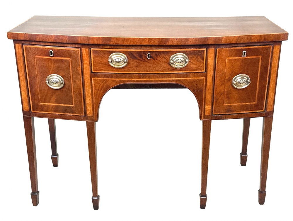 An 18th-century Georgian mahogany bowfront sideboard featuring a gently curved front, satinwood inlay, brass oval handles, and square tapered legs with spade feet. View IX