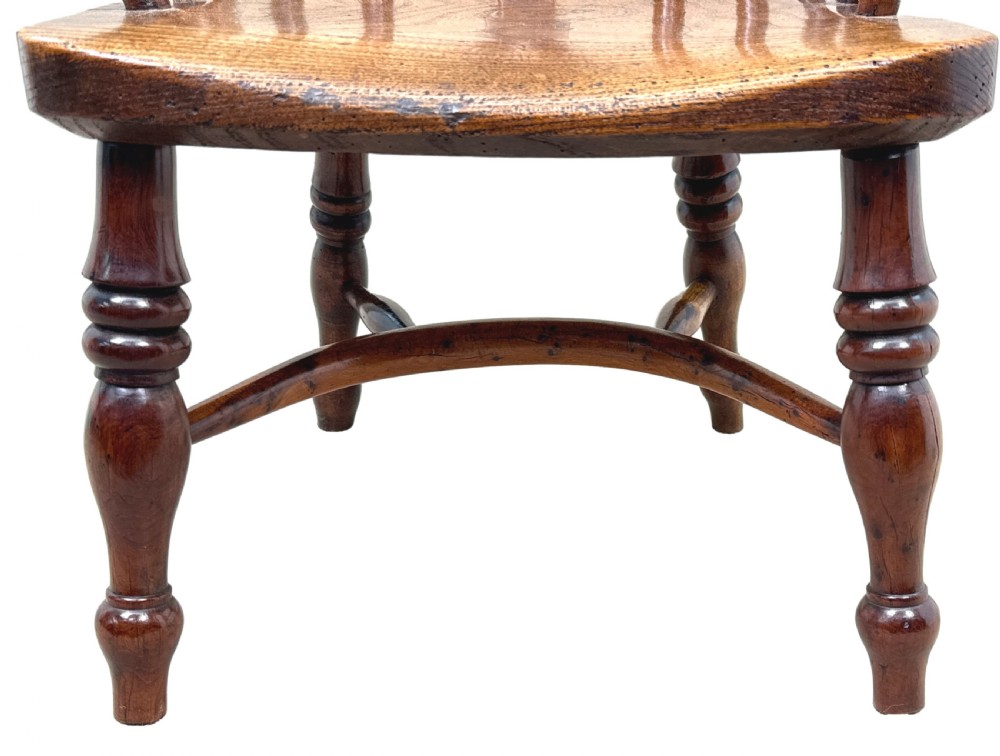 An antique child-sized Windsor armchair made of warm brown wood with turned legs, a hoop back, and a central pierced splat. View IV