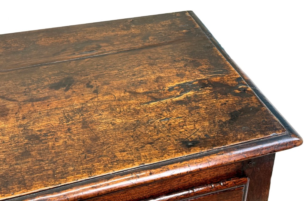An 18th-century dark oak dresser base featuring multiple drawers with pierced brass handles, turned front legs, and a lower pot board shelf. View V