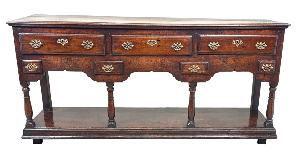 An 18th-century dark oak dresser base featuring multiple drawers with pierced brass handles, turned front legs, and a lower pot board shelf. View XIII