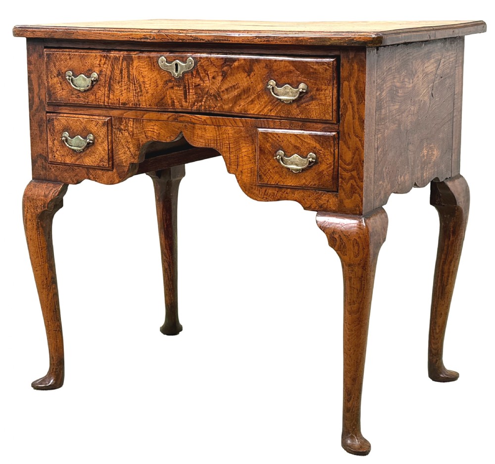 An 18th-century Georgian quilted elm lowboy featuring three drawers with brass handles, a shaped kneehole apron, and four slender cabriole legs.