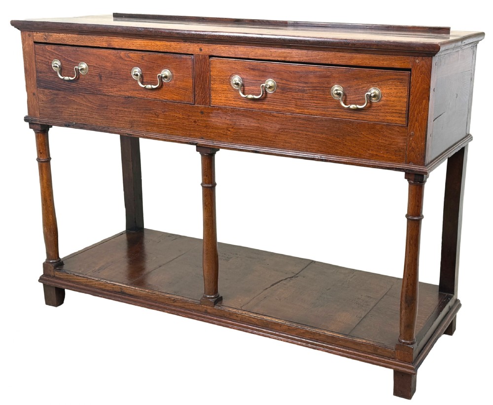 A late 18th-century Georgian oak dresser base featuring two drawers with brass swan-neck handles, turned front legs, and a lower pot board shelf.
