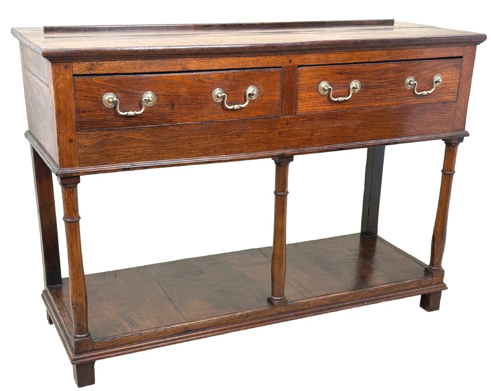 A late 18th-century Georgian oak dresser base featuring two drawers with brass swan-neck handles, turned front legs, and a lower pot board shelf. View XIII
