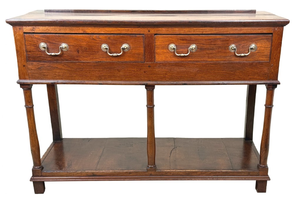A late 18th-century Georgian oak dresser base featuring two drawers with brass swan-neck handles, turned front legs, and a lower pot board shelf. View XIV