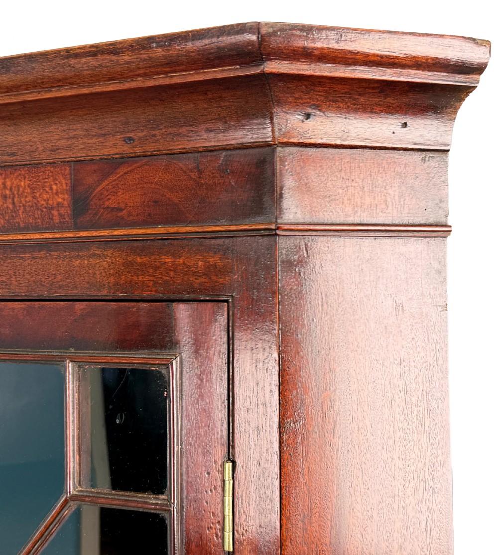 A tall two-part Georgian mahogany corner cabinet featuring upper astragal glazed doors and panelled lower doors. View IV