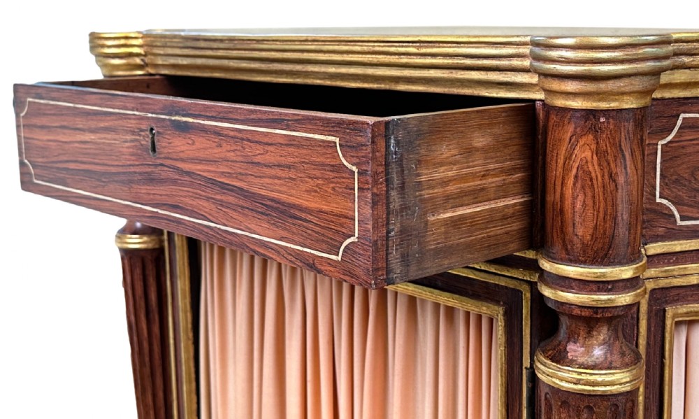 An antique Regency style breakfront side cabinet featuring simulated rosewood finishing, gold leaf gilded columns, and doors set with pleated pink fabric. View II