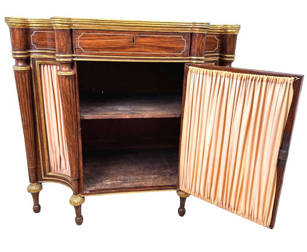 An antique Regency style breakfront side cabinet featuring simulated rosewood finishing, gold leaf gilded columns, and doors set with pleated pink fabric. View III