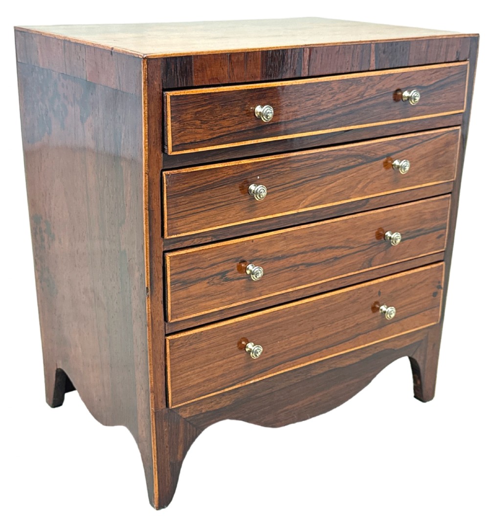 A Georgian rosewood miniature chest of four graduated drawers featuring stringing inlay and small round knob pulls. View X