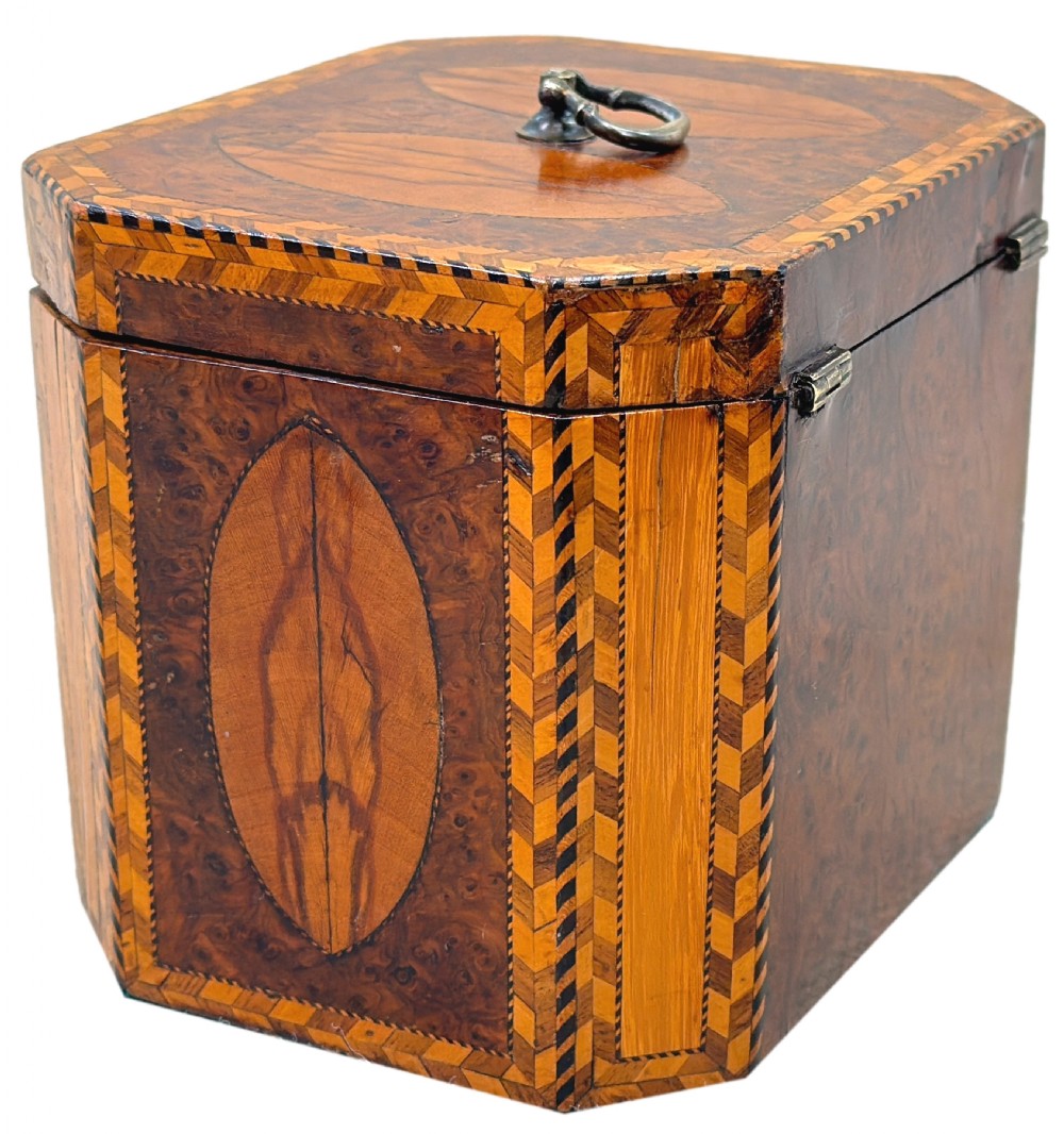 An 18th-century octagonal Georgian tea caddy crafted from burr yew wood with chevron stringing, oval marquetry panels, a brass top handle, and a brass keyhole escutcheon. View VII