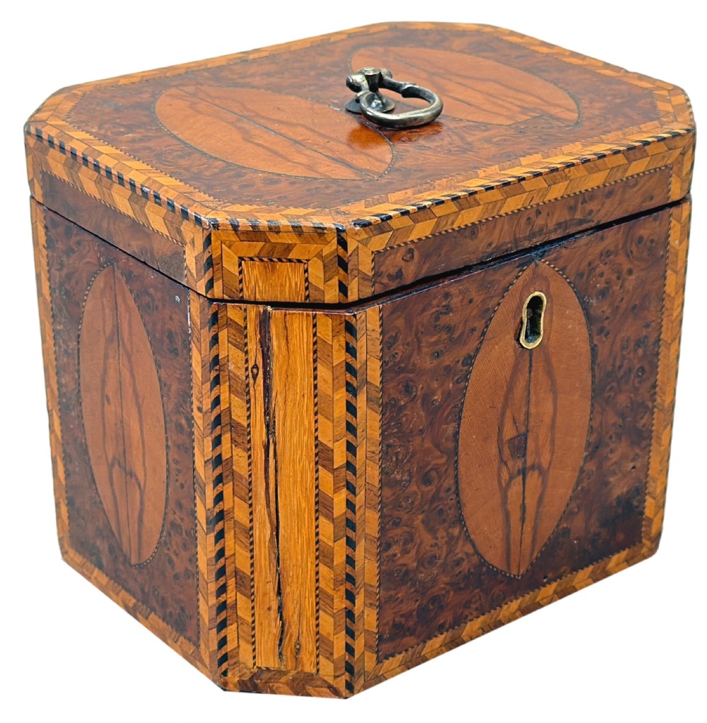An 18th-century octagonal Georgian tea caddy crafted from burr yew wood with chevron stringing, oval marquetry panels, a brass top handle, and a brass keyhole escutcheon. View VIII