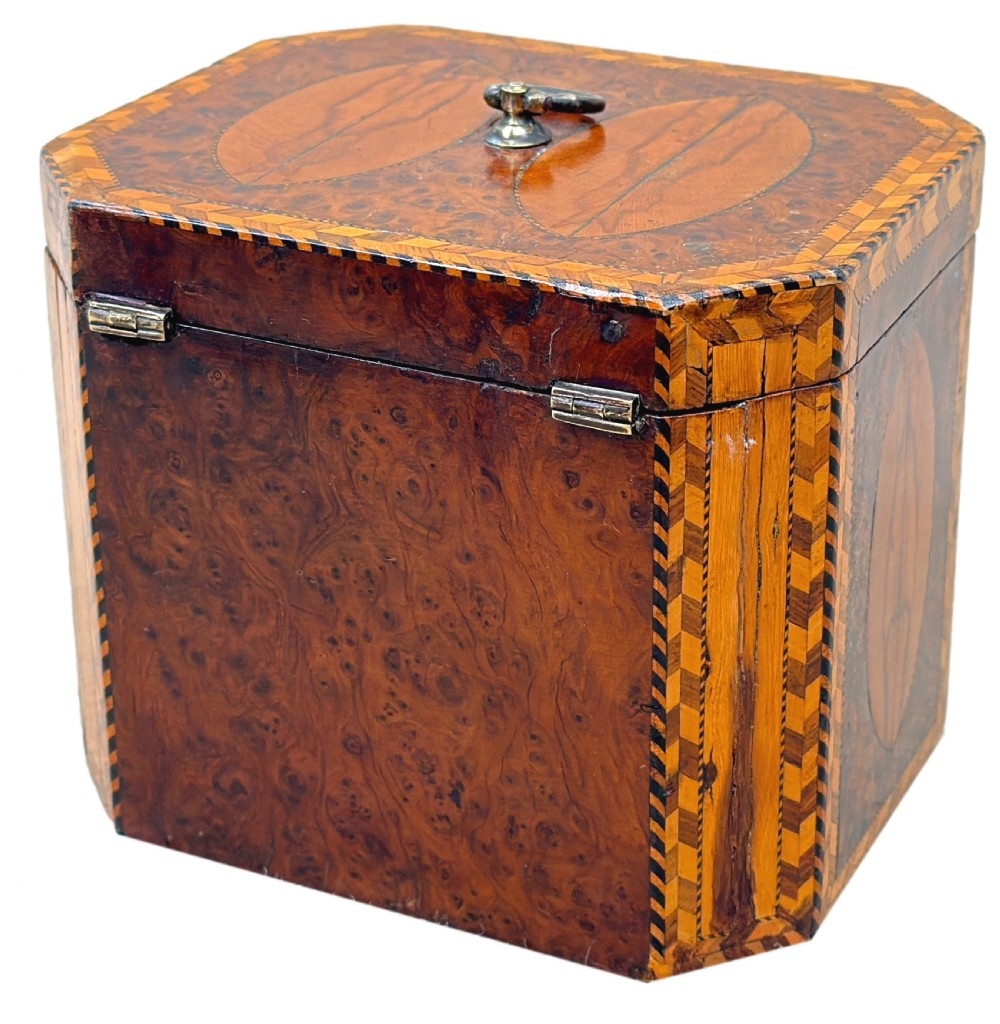 An 18th-century octagonal Georgian tea caddy crafted from burr yew wood with chevron stringing, oval marquetry panels, a brass top handle, and a brass keyhole escutcheon. View X