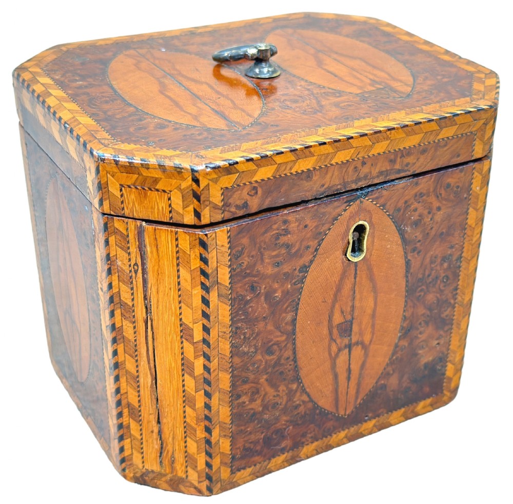 An 18th-century octagonal Georgian tea caddy crafted from burr yew wood with chevron stringing, oval marquetry panels, a brass top handle, and a brass keyhole escutcheon. View XII