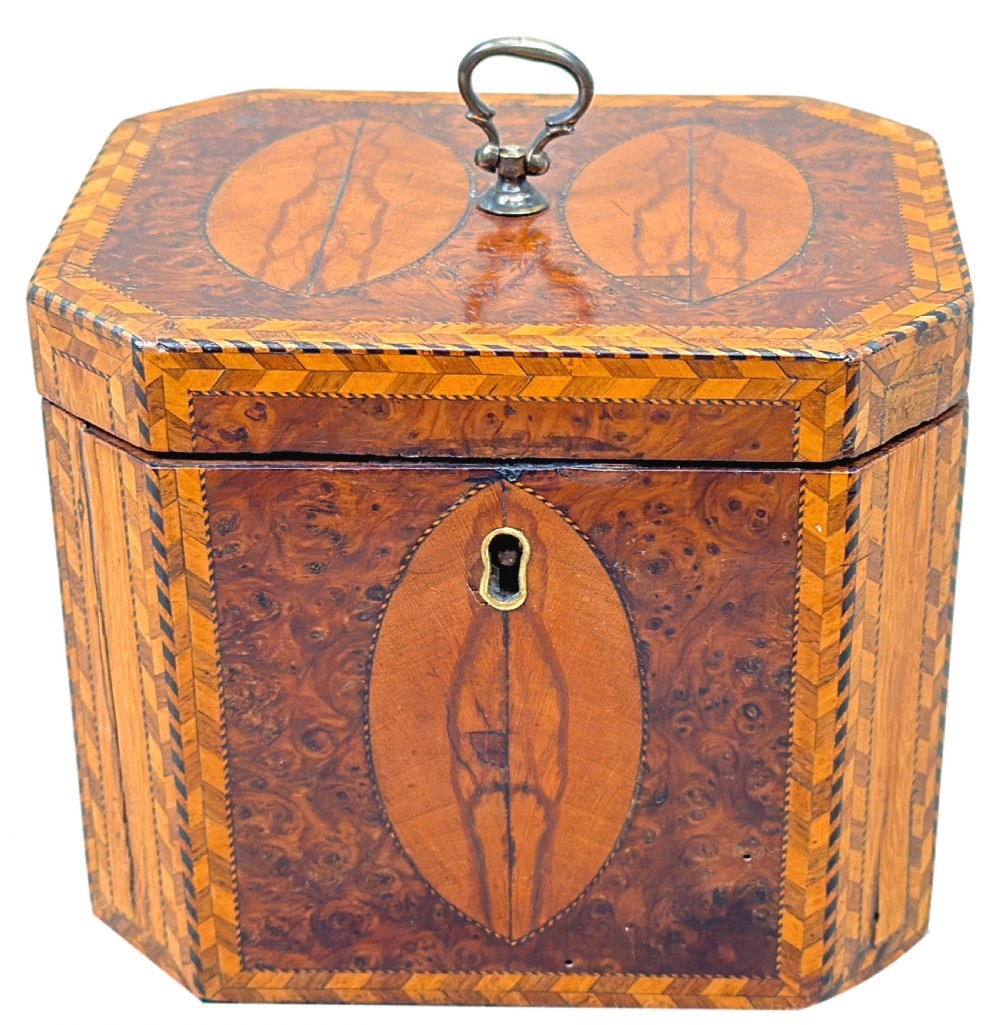 An 18th-century octagonal Georgian tea caddy crafted from burr yew wood with chevron stringing, oval marquetry panels, a brass top handle, and a brass keyhole escutcheon. View XIII