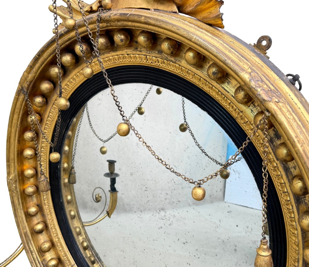 A circular Regency giltwood convex mirror topped with a carved eagle surmount, featuring an ebonised slip, ball moulding, and two twin candle sconces. View VI