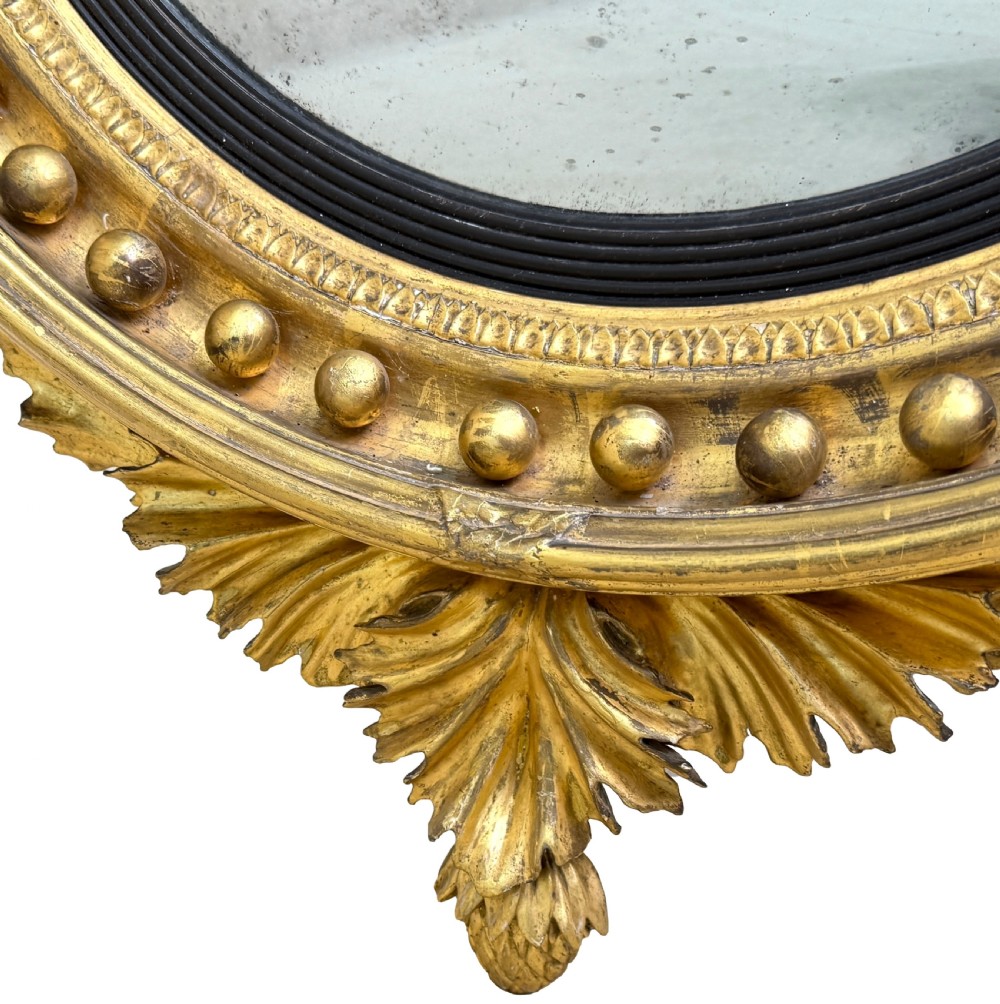 A circular Regency giltwood convex mirror topped with a carved eagle surmount, featuring an ebonised slip, ball moulding, and two twin candle sconces. View IX