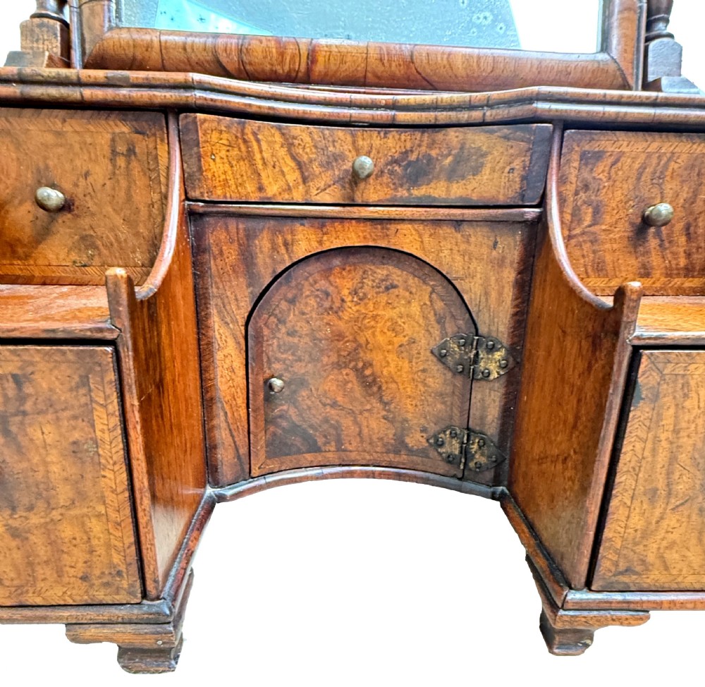 An early 18th-century Georgian walnut dressing table mirror featuring a shaped carved cresting, turned supports, and a base with miniature drawers and a central arch. View V