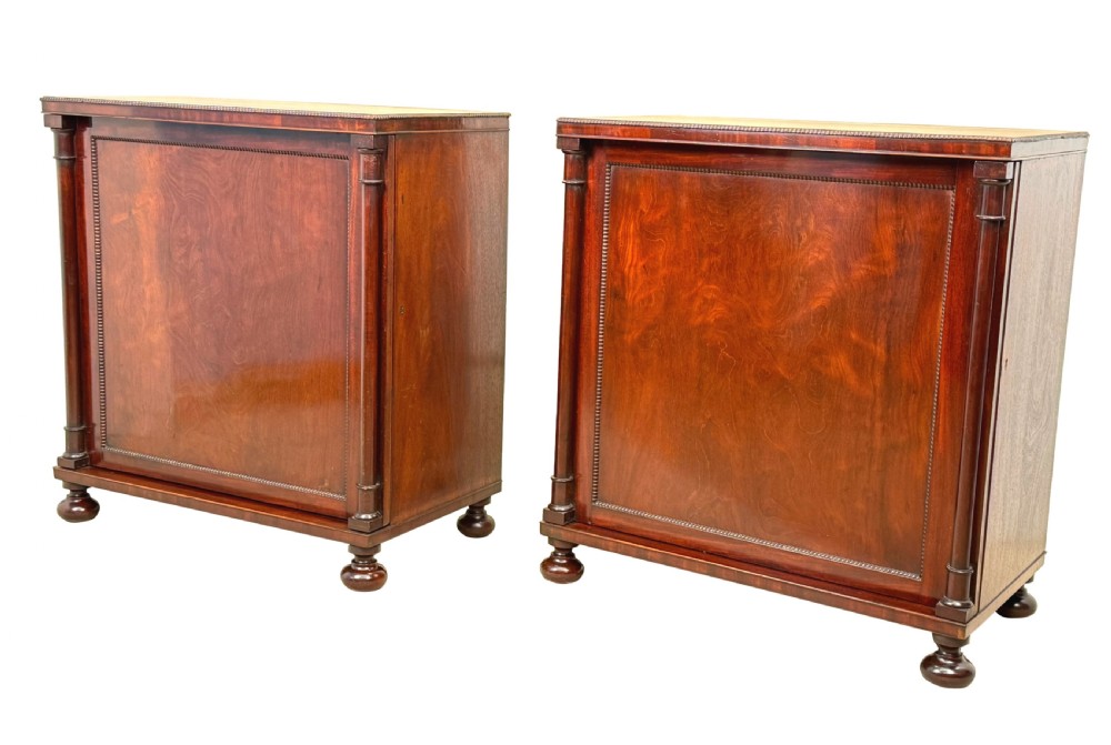 A pair of matching Regency mahogany side cupboards featuring flame veneer panel doors, flanking columns, and turned ball feet.