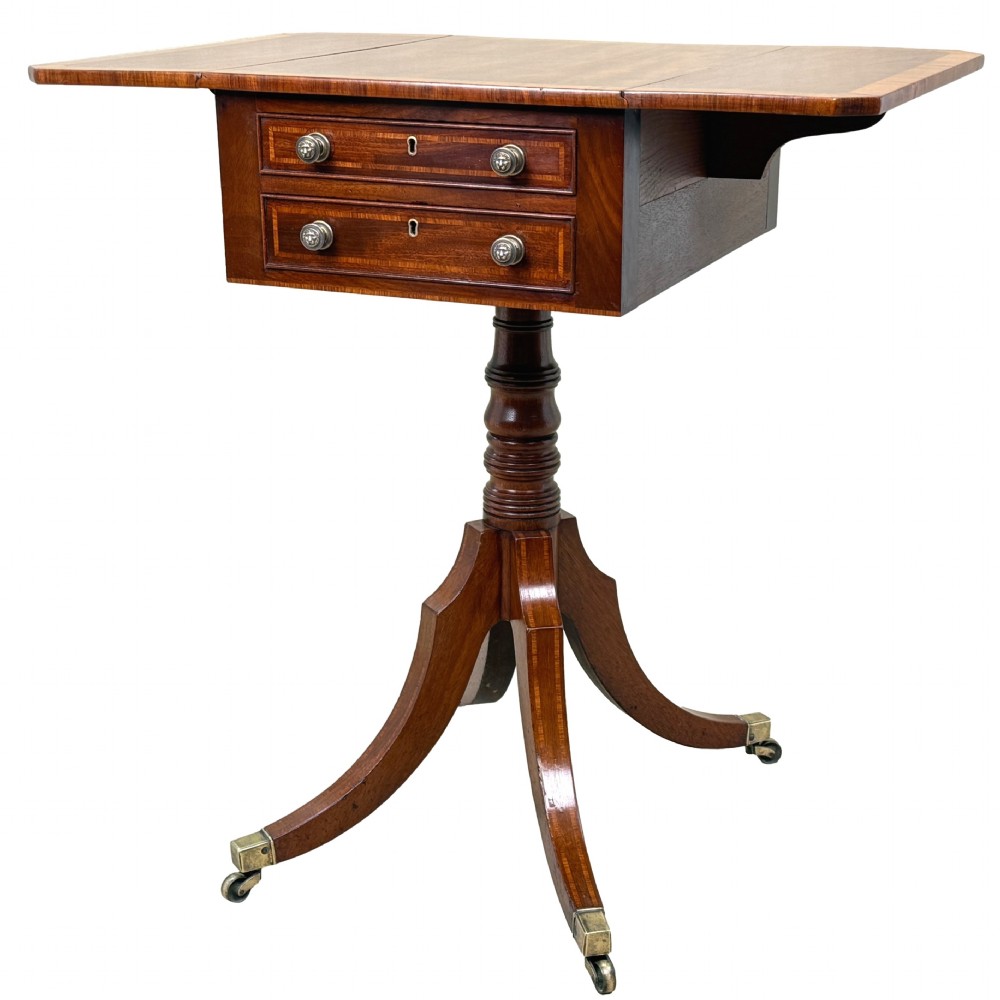 A Georgian mahogany baby Pembroke table with two drop leaves, double drawers with inlay, a turned central pedestal, and sabre tripod legs on brass castors.