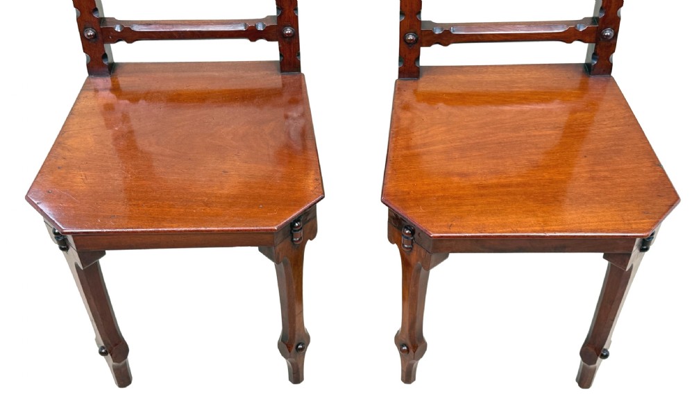 A pair of Victorian mahogany hall chairs featuring carved shield backrests, open architectural arches, turned finials, and solid wooden seats. View II