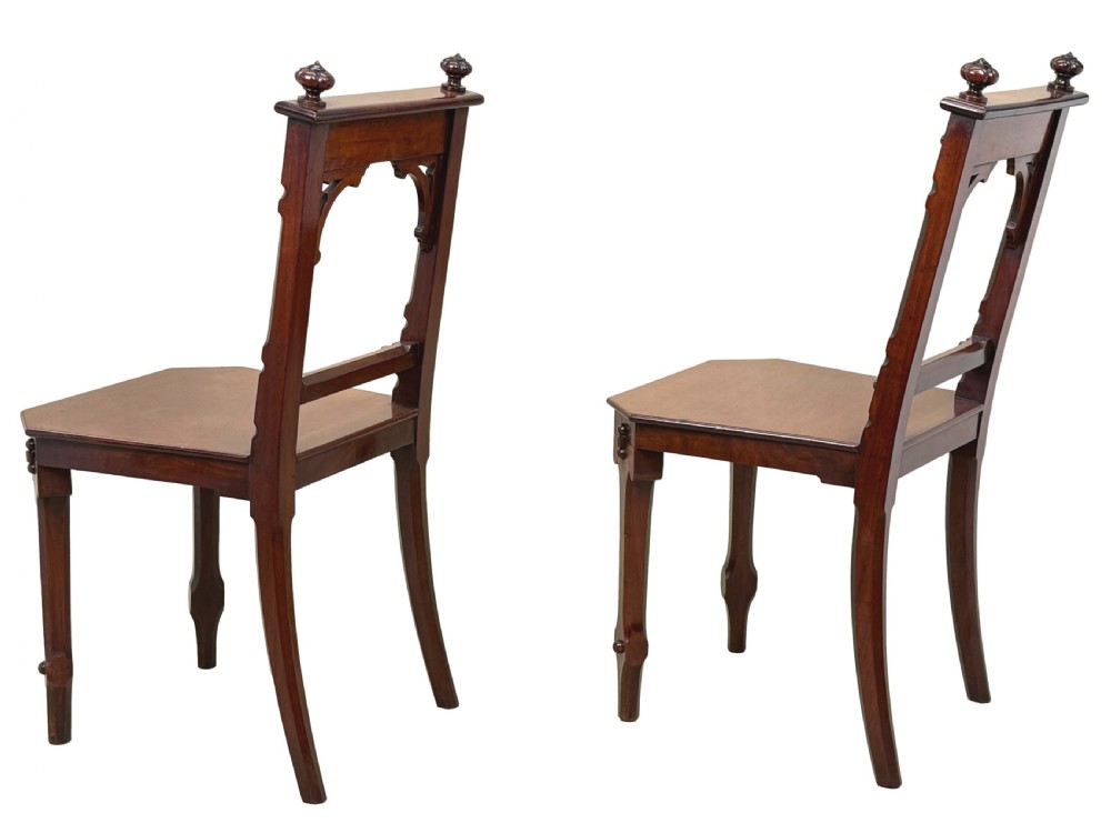 A pair of Victorian mahogany hall chairs featuring carved shield backrests, open architectural arches, turned finials, and solid wooden seats. View III