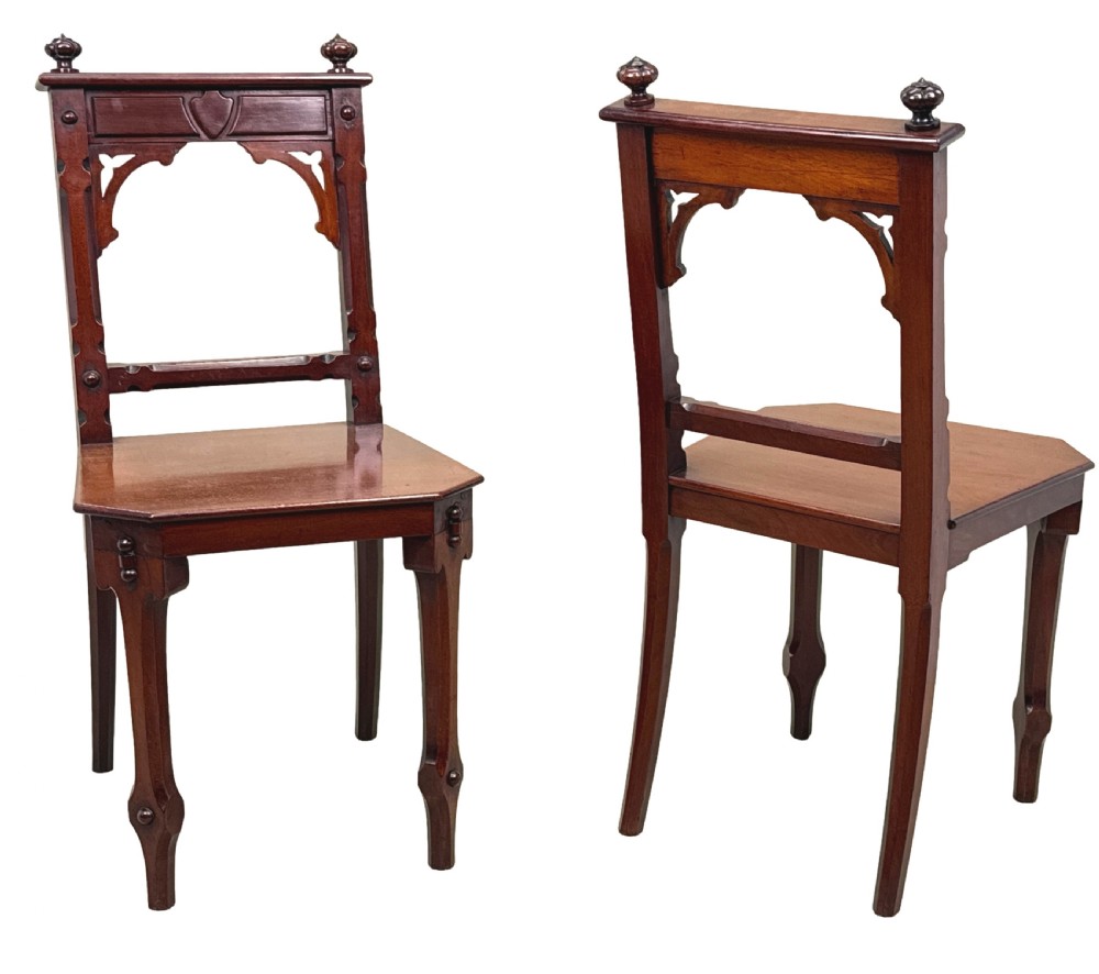 A pair of Victorian mahogany hall chairs featuring carved shield backrests, open architectural arches, turned finials, and solid wooden seats. View IV