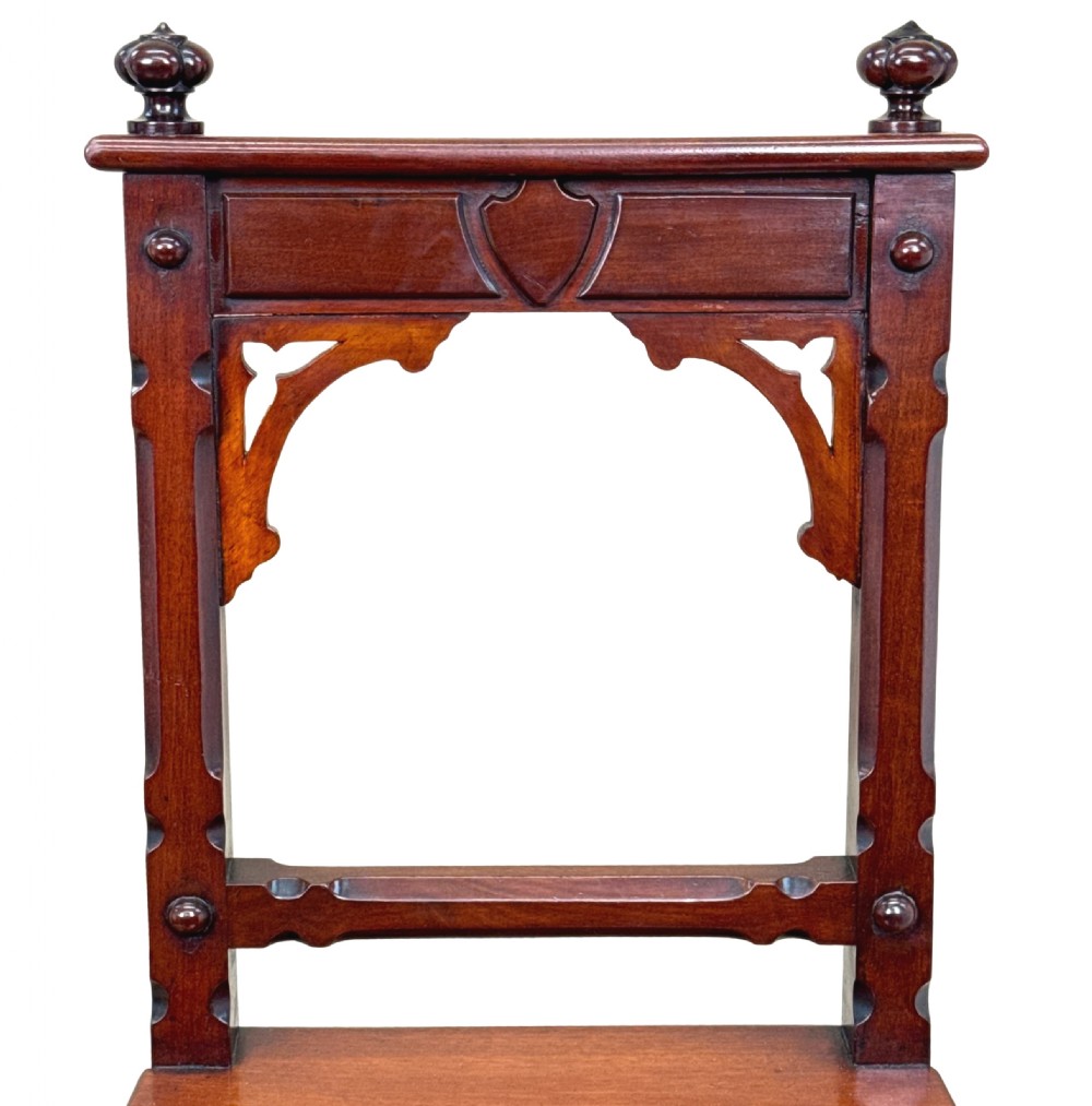 A pair of Victorian mahogany hall chairs featuring carved shield backrests, open architectural arches, turned finials, and solid wooden seats. View V
