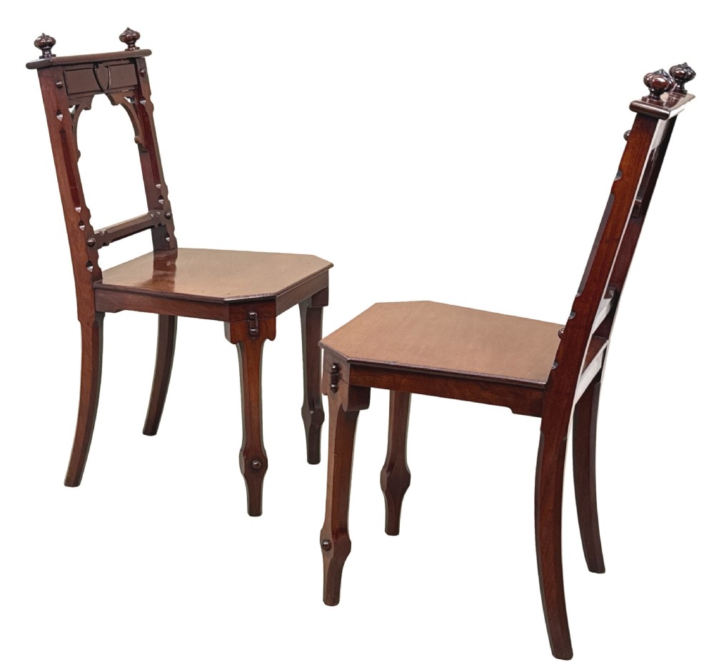 A pair of Victorian mahogany hall chairs featuring carved shield backrests, open architectural arches, turned finials, and solid wooden seats. View VI