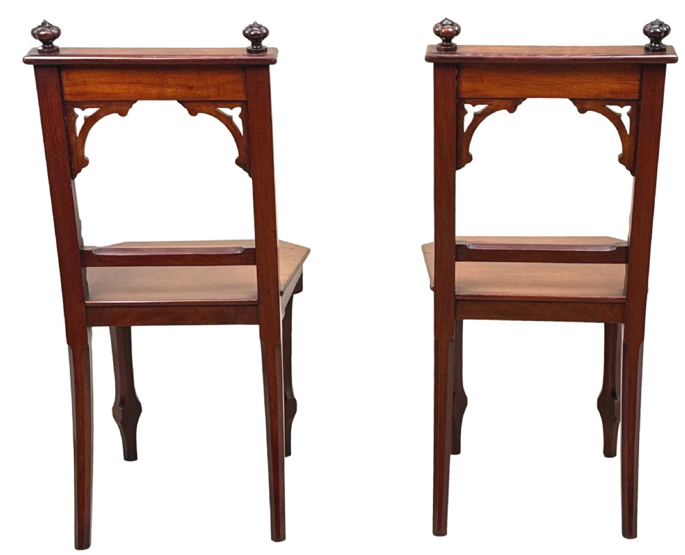 A pair of Victorian mahogany hall chairs featuring carved shield backrests, open architectural arches, turned finials, and solid wooden seats. View IX