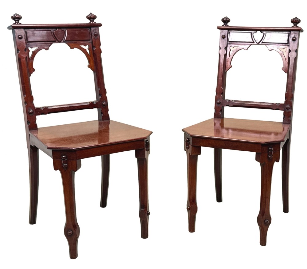 A pair of Victorian mahogany hall chairs featuring carved shield backrests, open architectural arches, turned finials, and solid wooden seats. View XI
